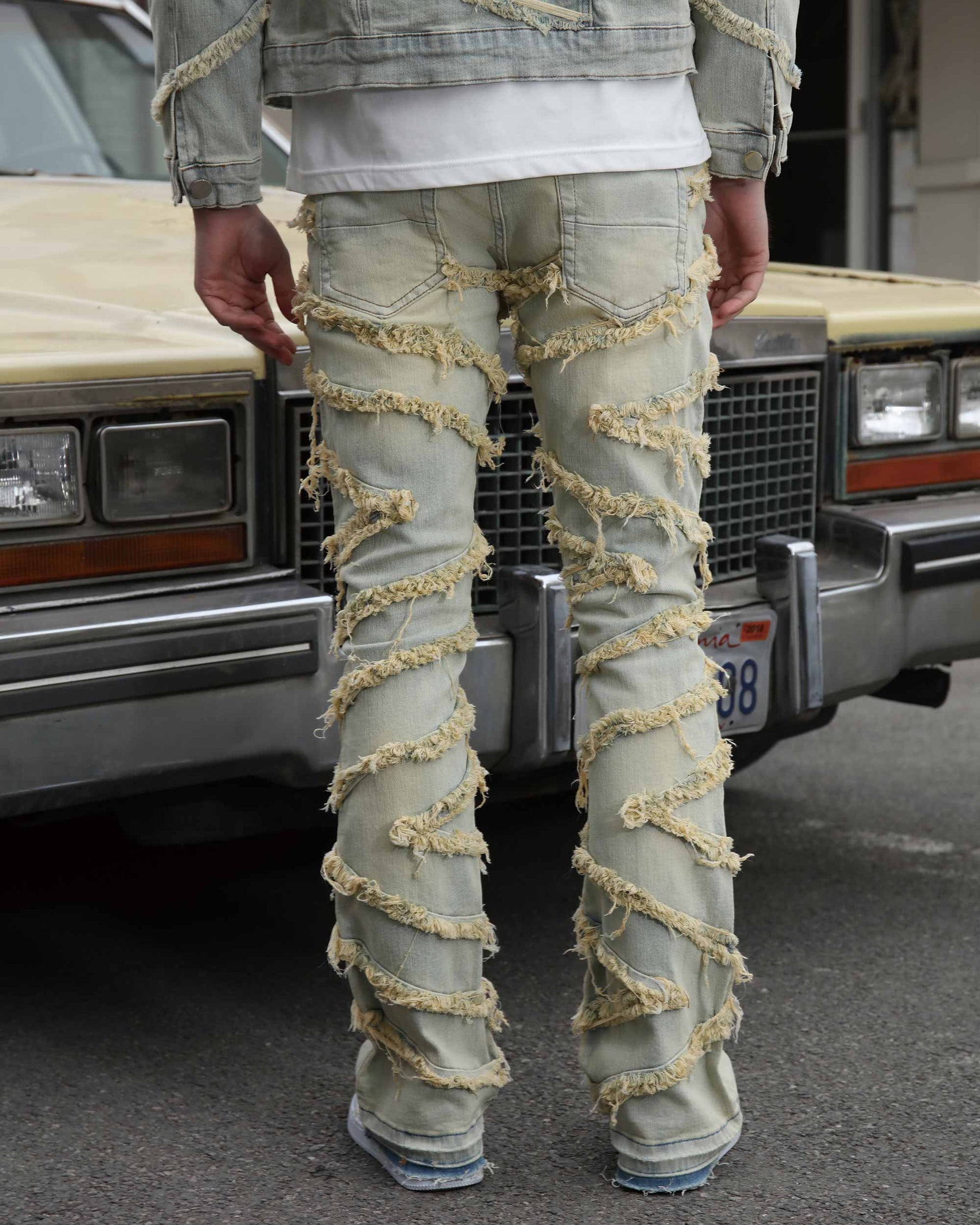 Men wearing LOGEIQ light-wash vintage blue stacked patch flare jeans with bold frayed strips, standing in front of a classic vintage car outdoors.