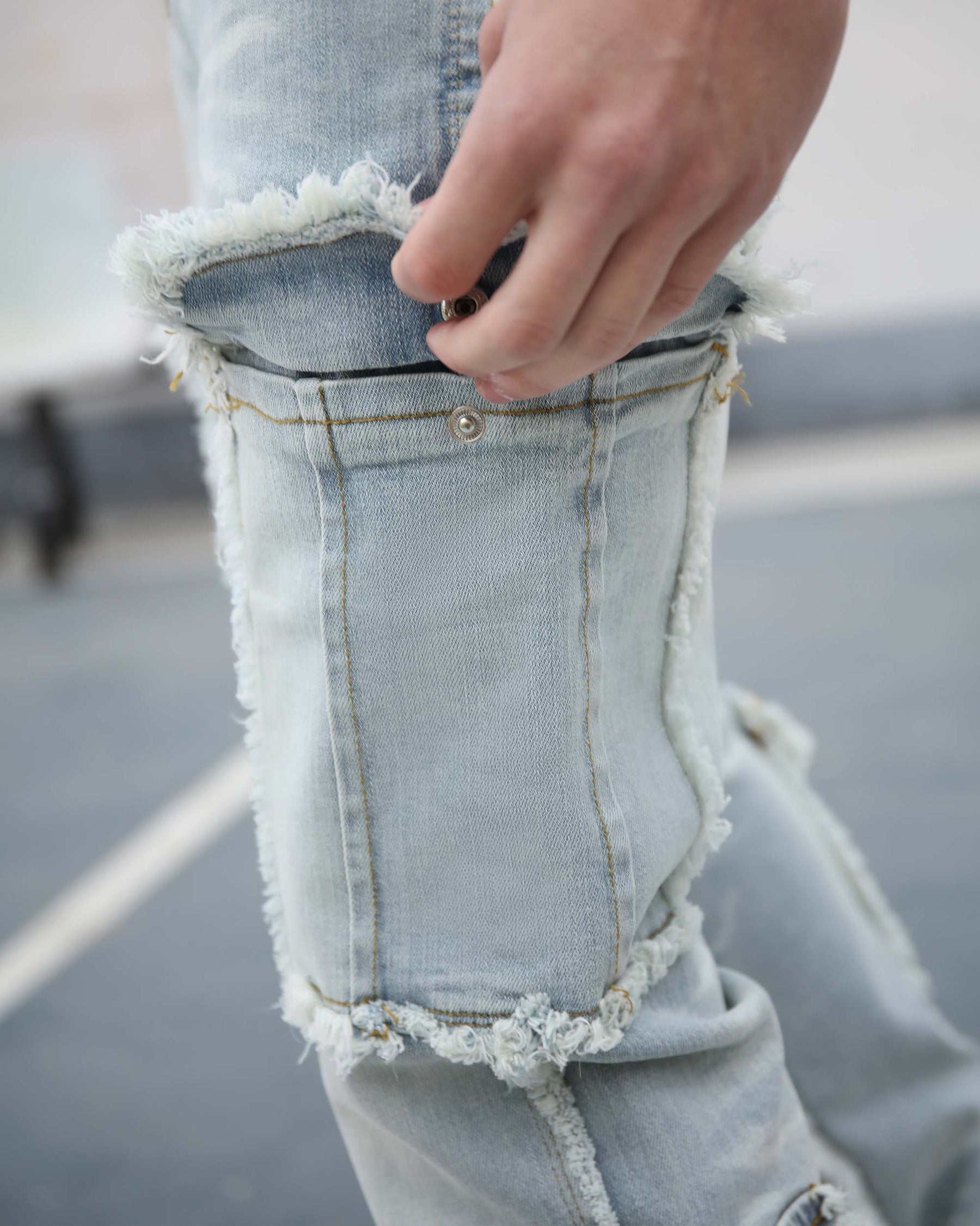 A close-up shows a hand opening a pocket on light blue, distressed jeans. The jeans have frayed edges and visible stitching