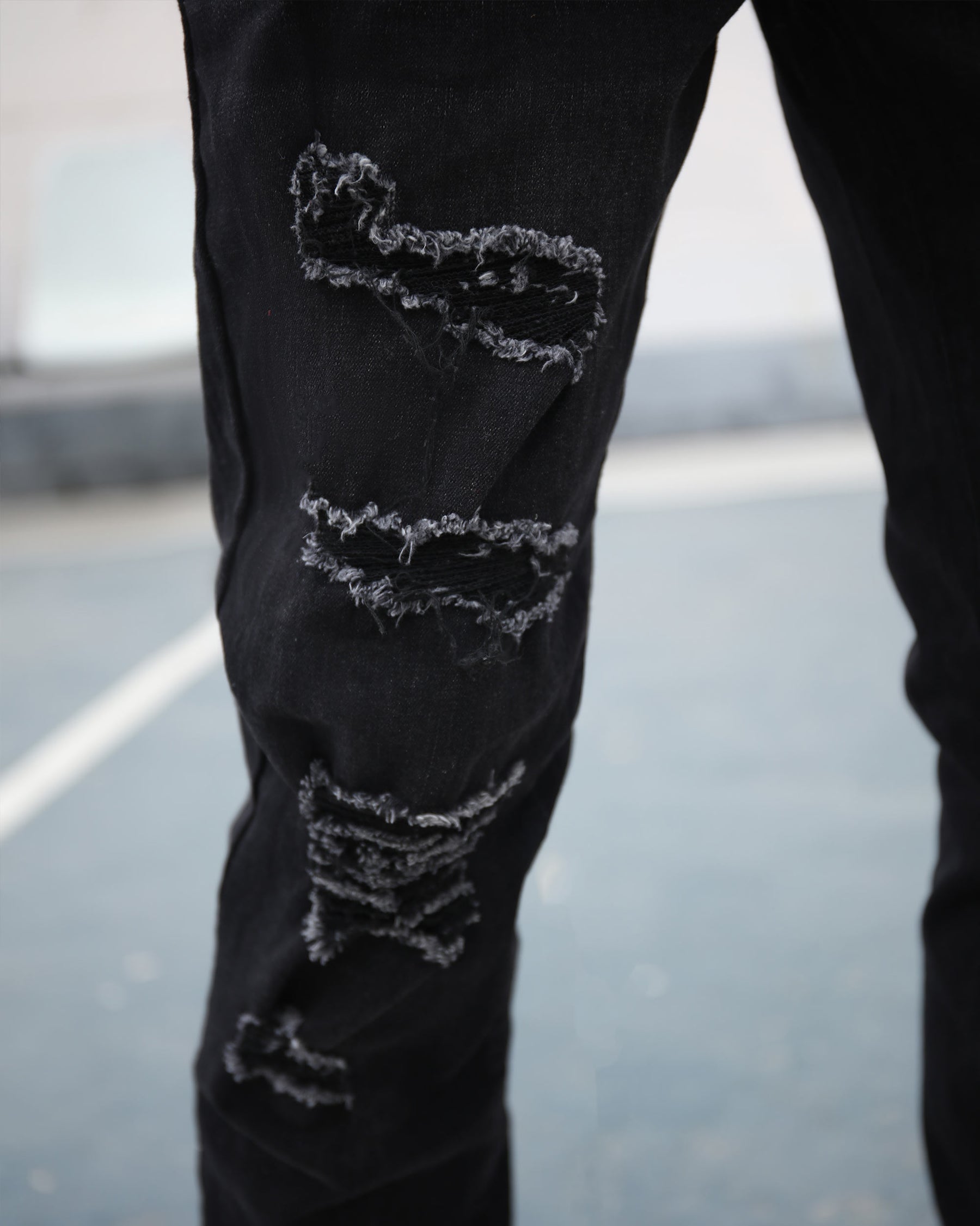 Close-up of LOGEQI men's black jeans with multiple frayed, distressed rips on the leg.