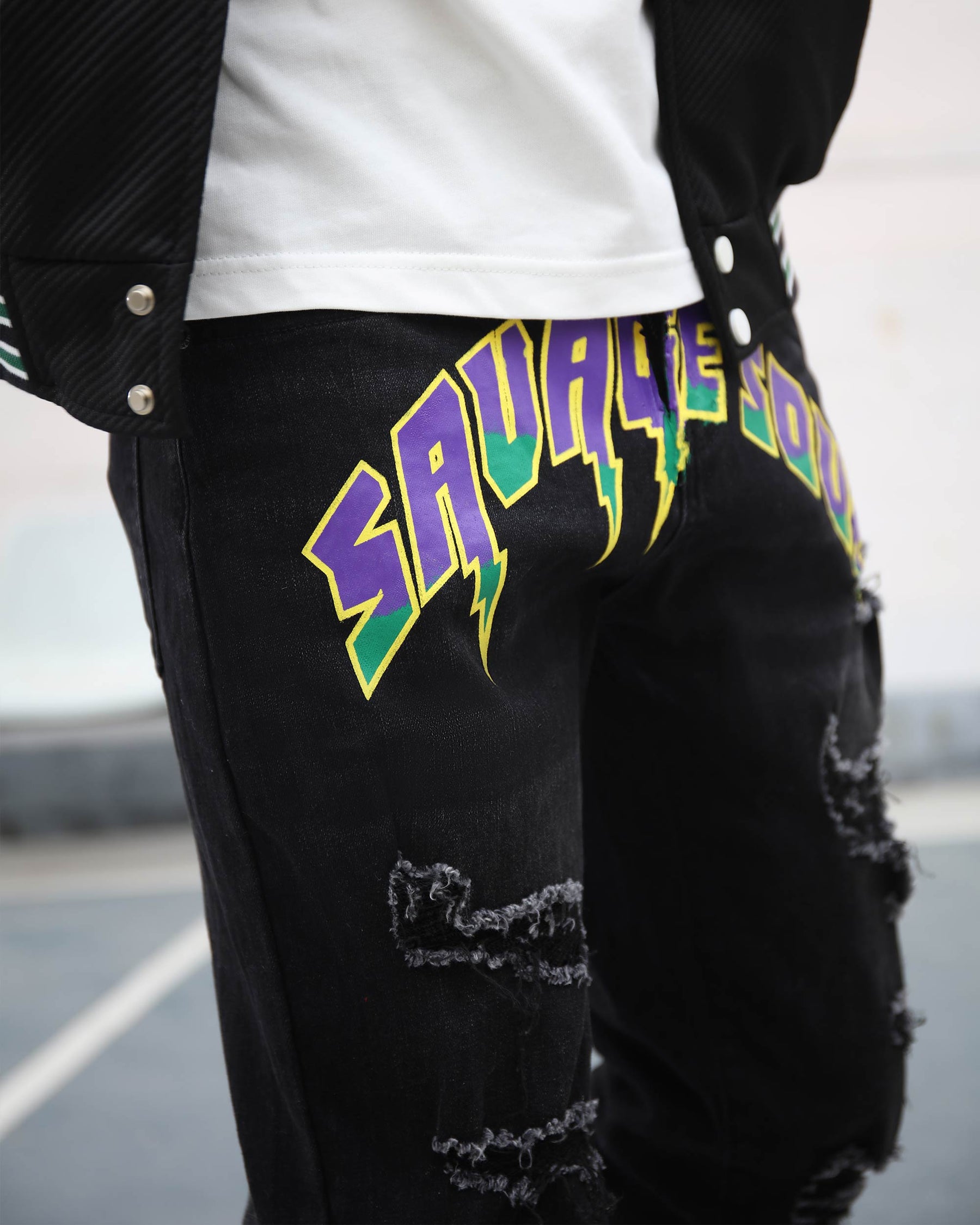 Close-up of LOGEQI black ripped jeans with colorful “SAVAGE SOUL” print, worn with a white shirt and jacket
