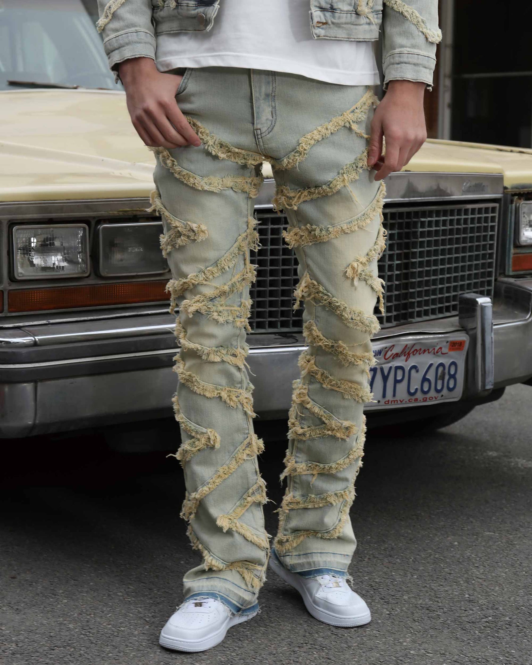 LOGEQI Men's Vintage Blue Stacked Patch Denim Jeans with extreme diagonal frayed strips, flared (bootcut), paired with white sneakers.