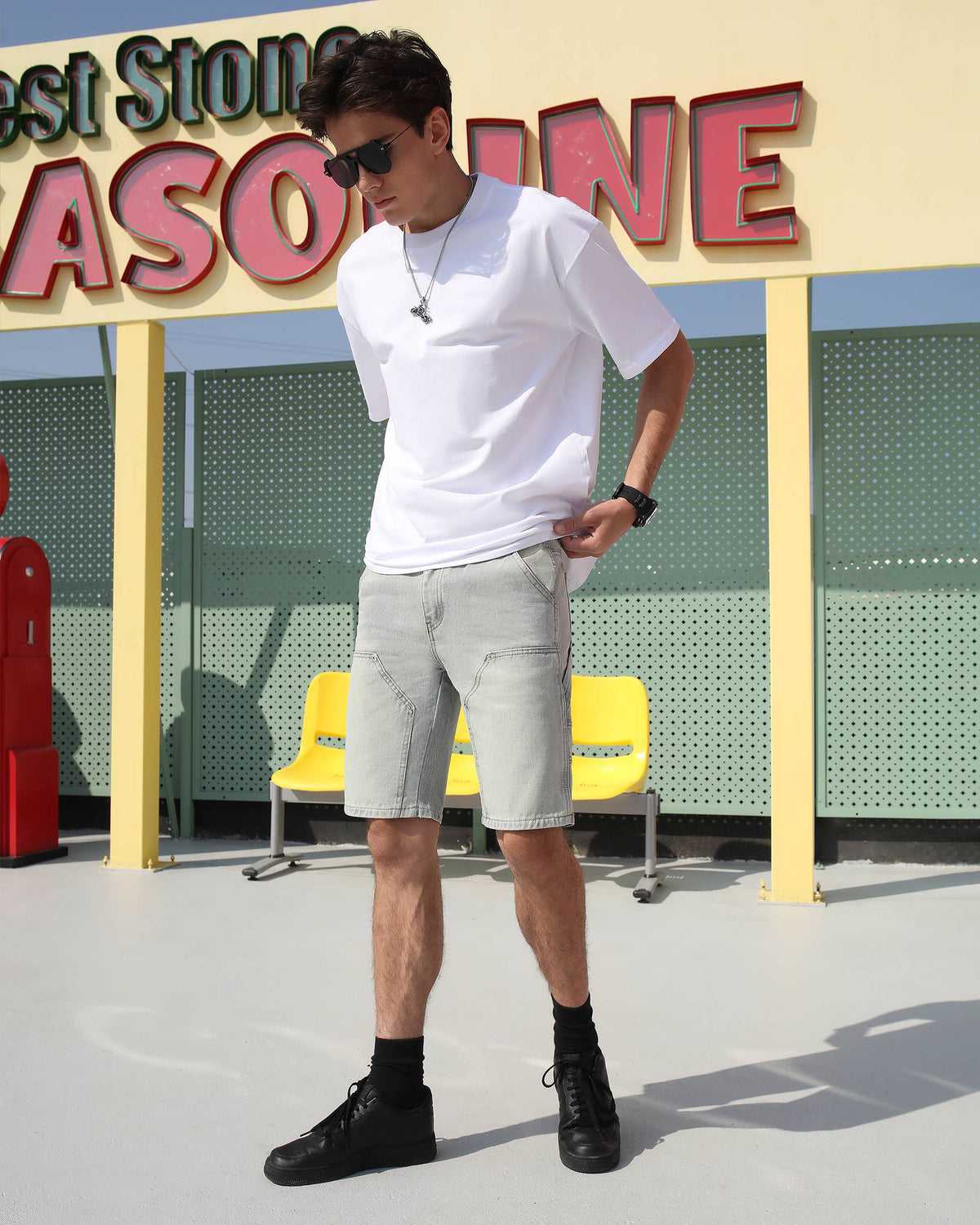 A man wearing LOGEQI's affordable distressed light blue denim jean shorts, paired with sunglasses, black shoes, and a white T-shirt on the street
