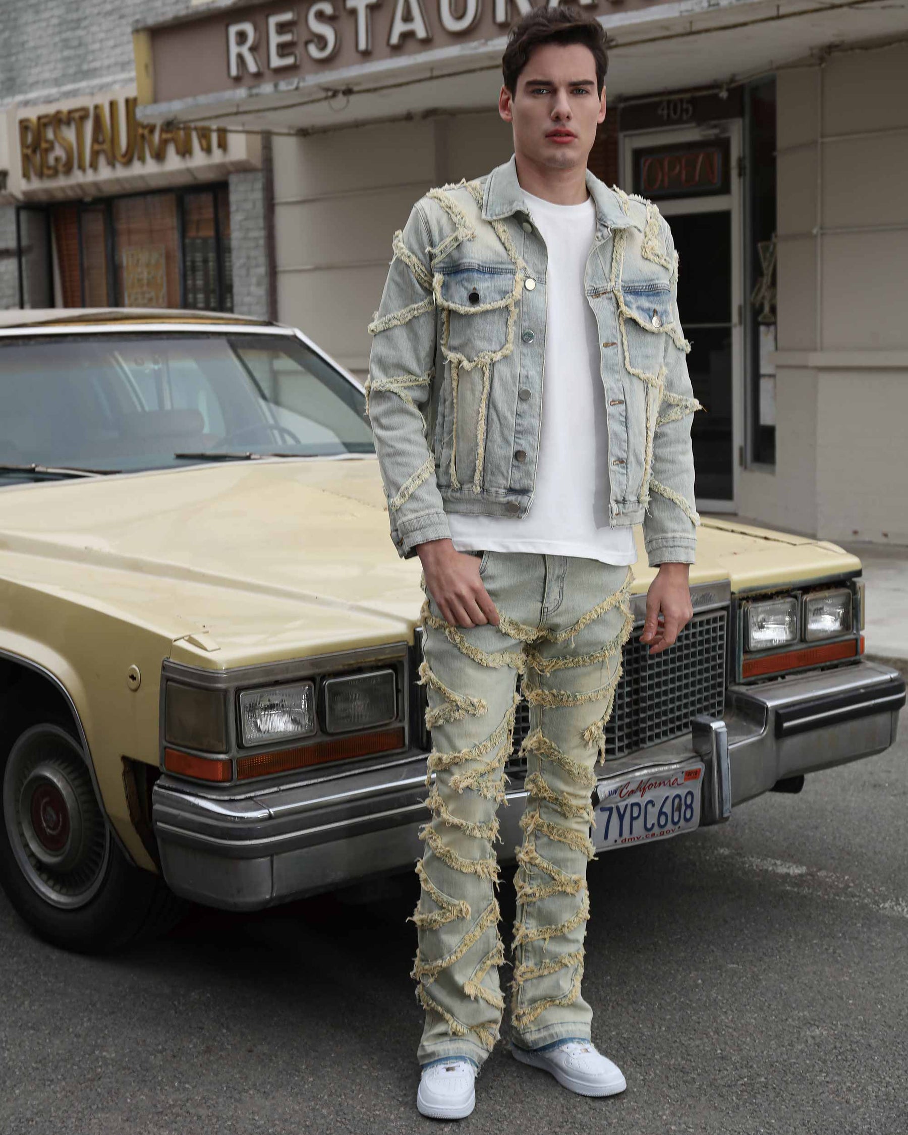 A man wearing LOGEQI Vintage Blue Stacked Patch Jeans with frayed strips and a LOGEQI denim jacket, standing in front of a vintage car.