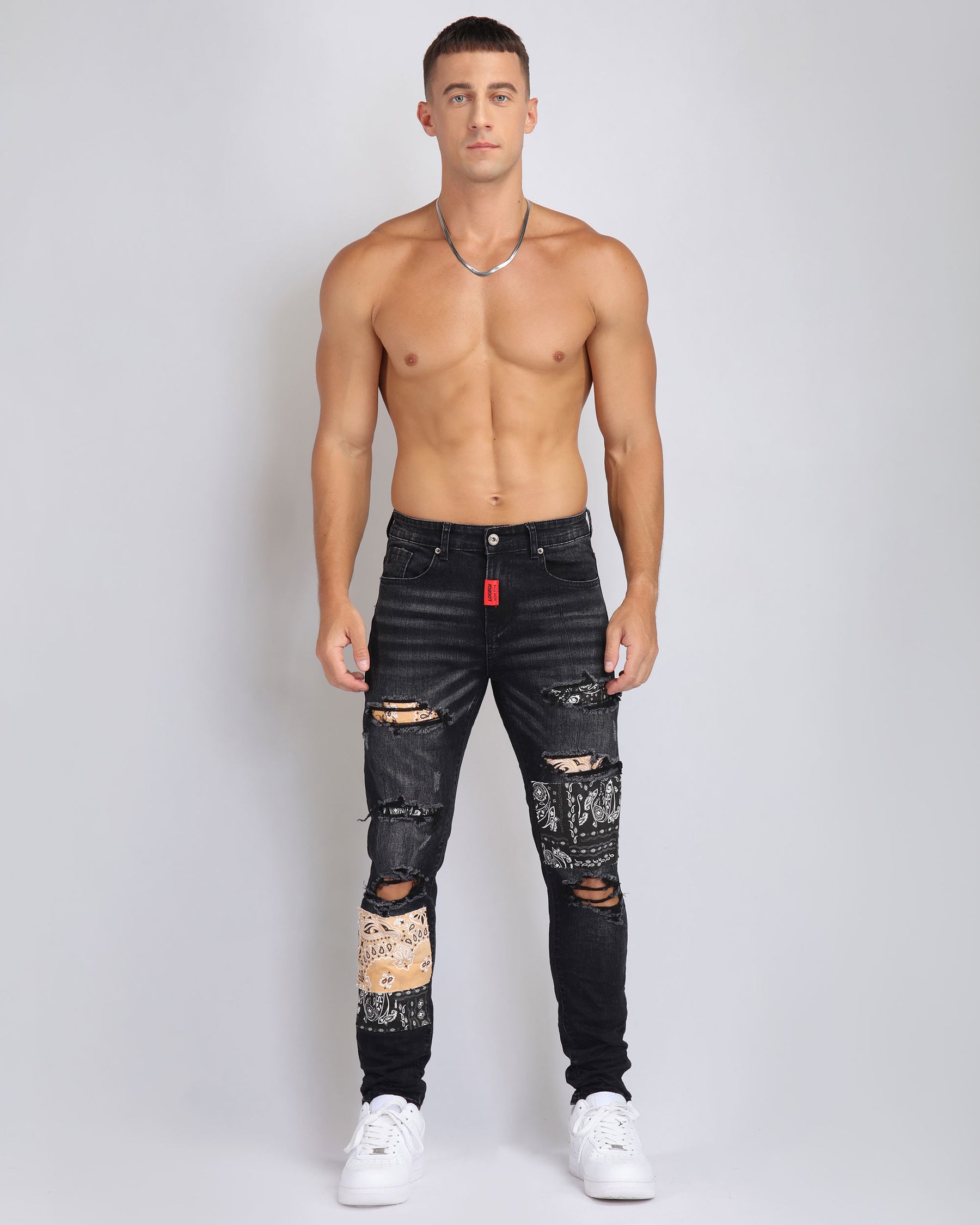 A shirtless man poses against a plain background, wearing LOGEQI black distressed ripped jeans with patchwork details and white sneakers, accessorized with a silver chain.