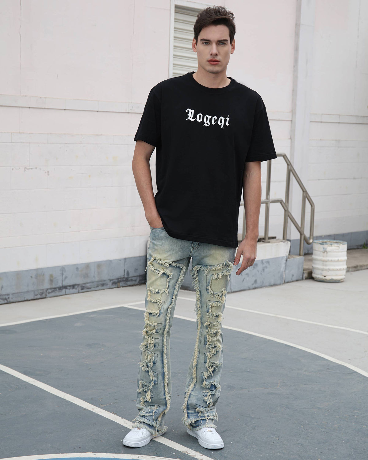A man stands on a court, wearing a LOGEQI black “Logeqi” tee, LOGEQI distressed jeans with stacked frayed patched designs, and white sneakers, with a building background.