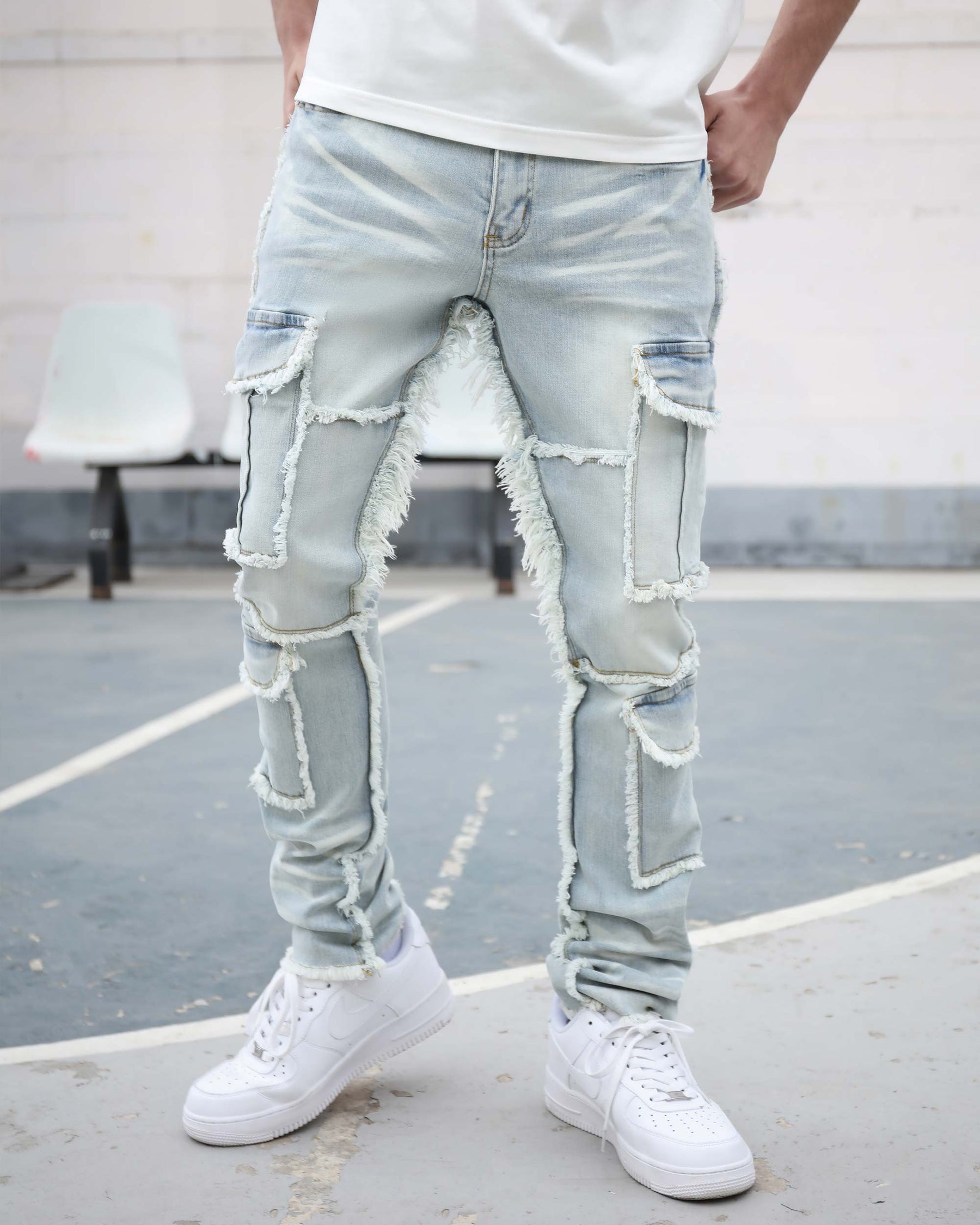 A man stands on a basketball court, wearing LOGEQI's light - wash distressed jeans with frayed patchwork details and white Nike Air Force 1 sneakers. A white tee and a simple background complete the casual, streetwear look