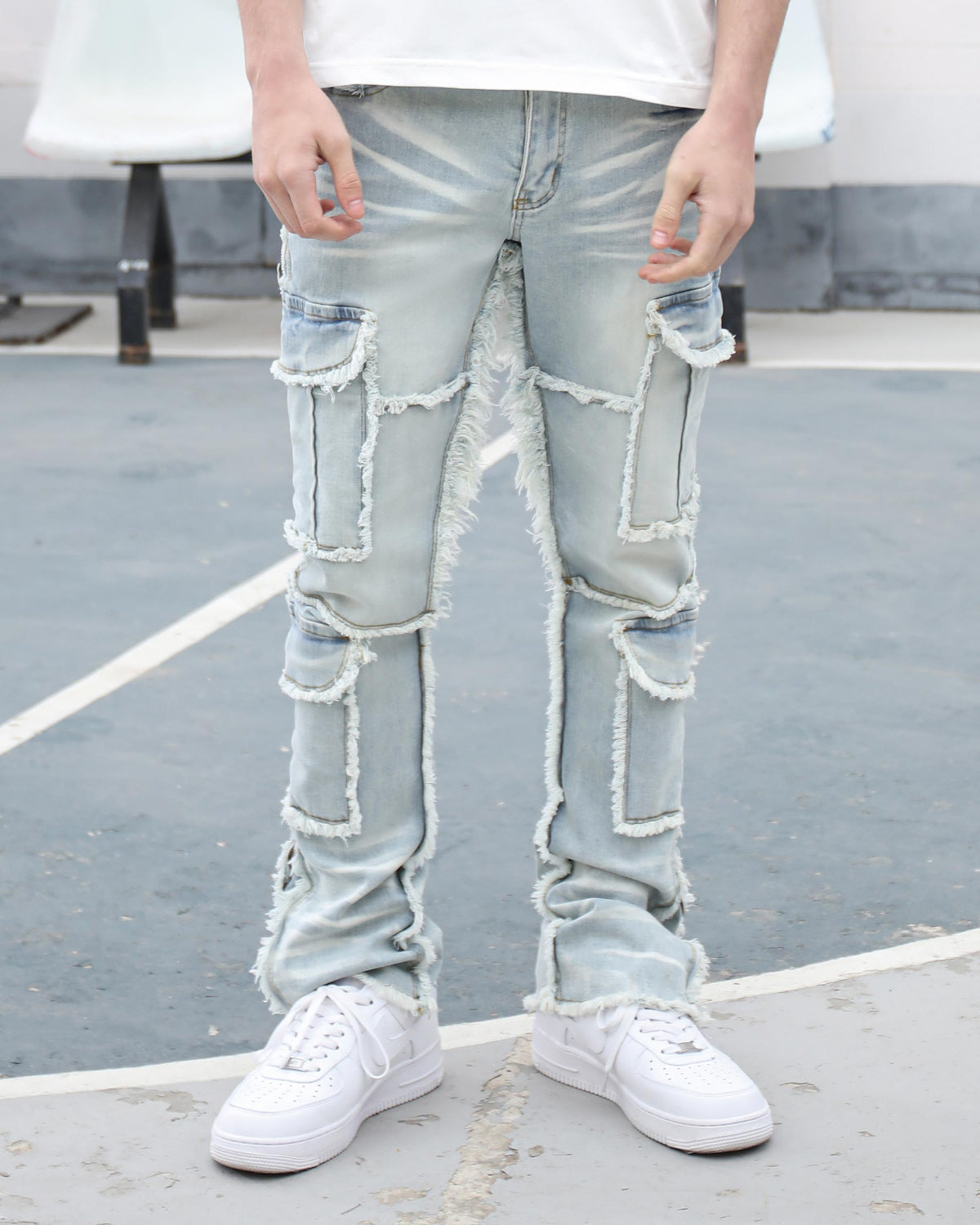 A man wearing LOGEQI light blue distressed denim jeans with frayed patch pockets, paired with white sneakers, showcasing streetwear fashion on a pavement