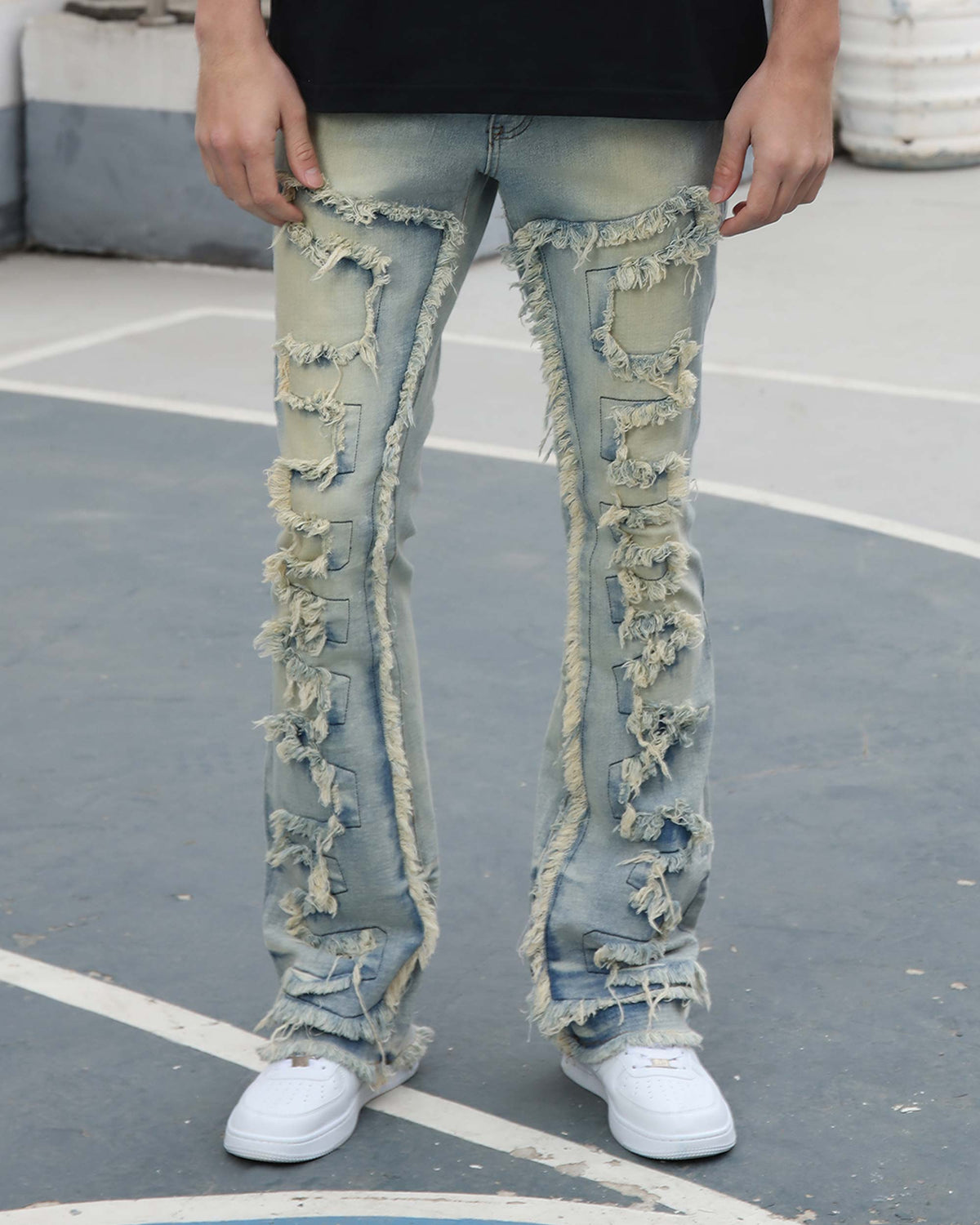 A man wearing LOGEQI light-wash, heavily distressed flared jeans with frayed patches, paired with white sneakers, on a paved area.