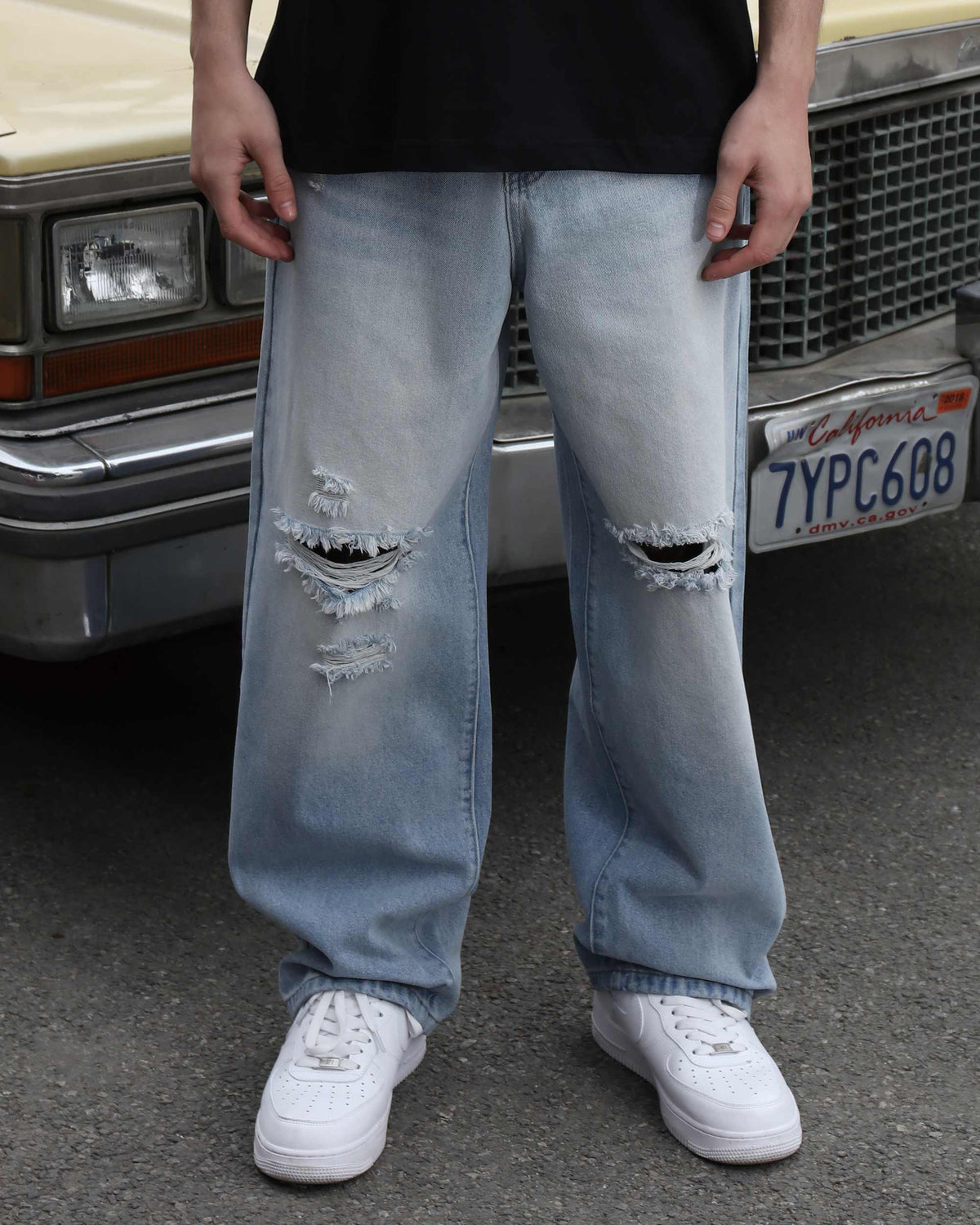 A man wearing LOGEQI's knee-ripped, distressed baggy jeans in a loose fit, standing in front of a car