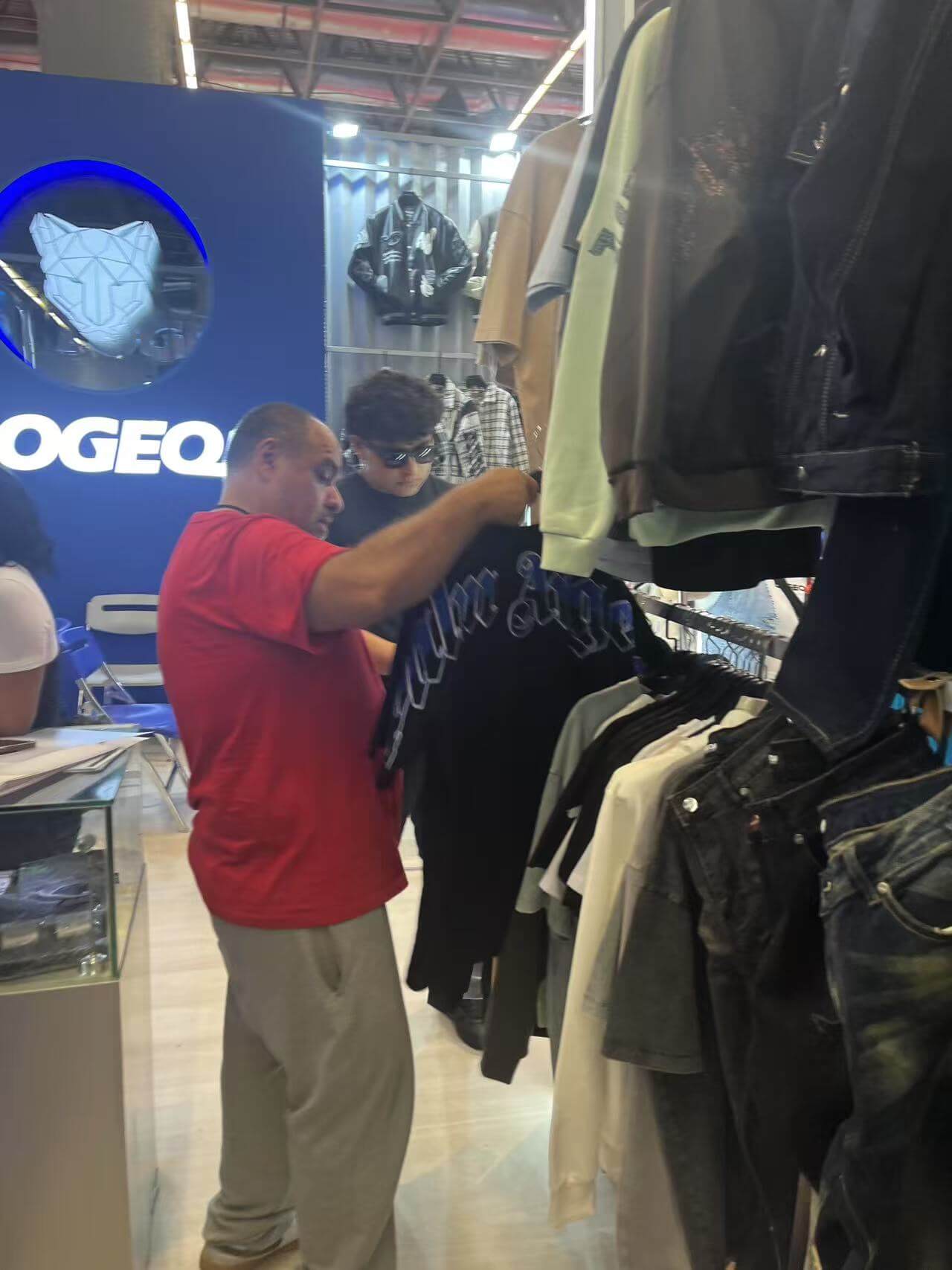 Customers taking a close look at LOGEQI graphic tees at INTERMODA 2025