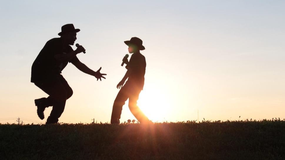 Father - son duo singing silhouette against sunset backdrop on a meadow - heartwarming family moment