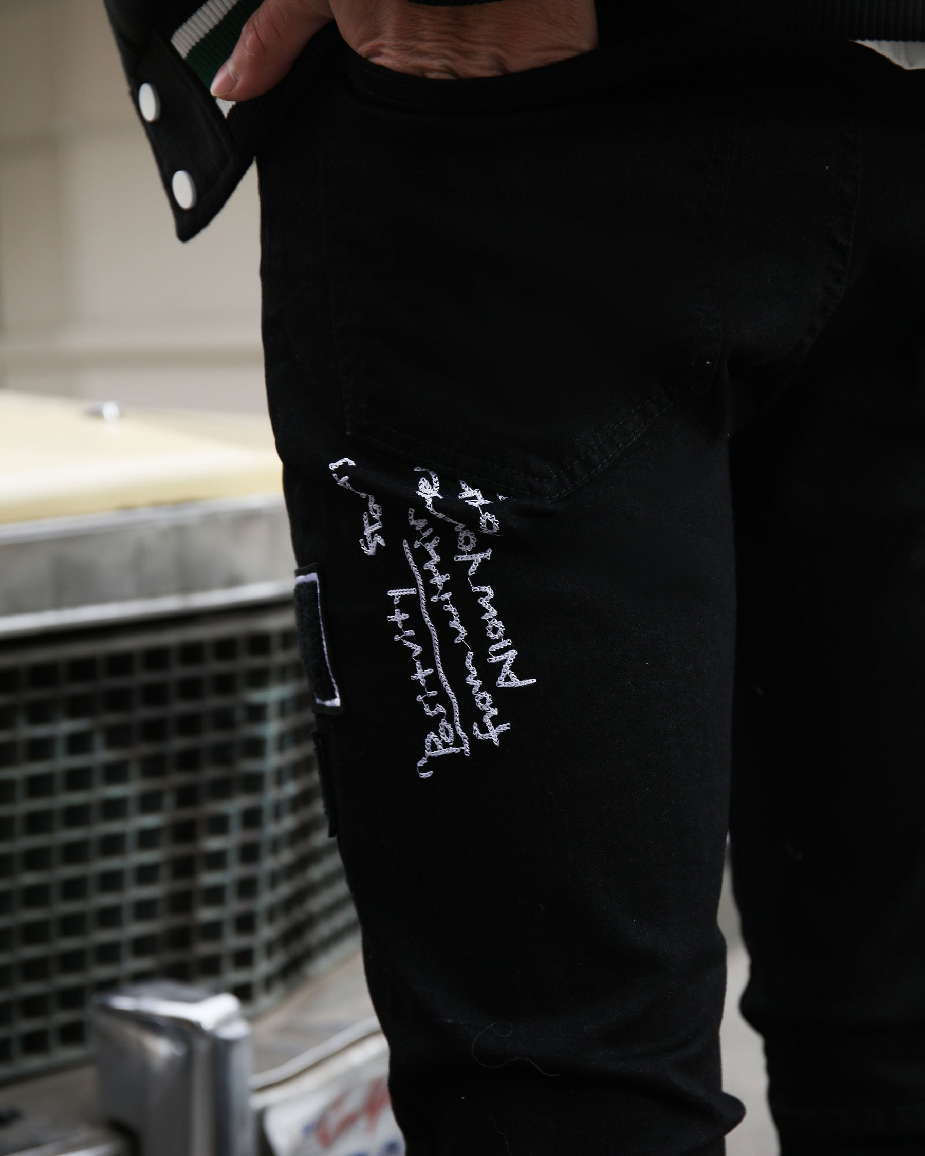 Black jeans featuring white embroidered phrases, hand in pocket, urban style