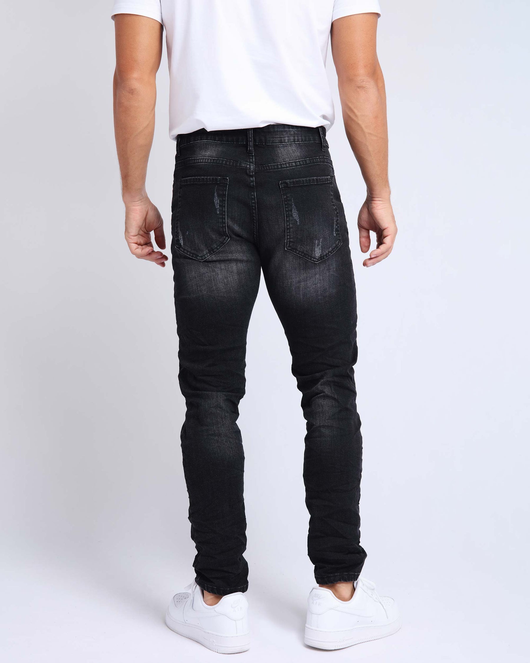 A man wearing LOGEQI black ripped distressed jeans, a white tee, and white sneakers, rear view.
