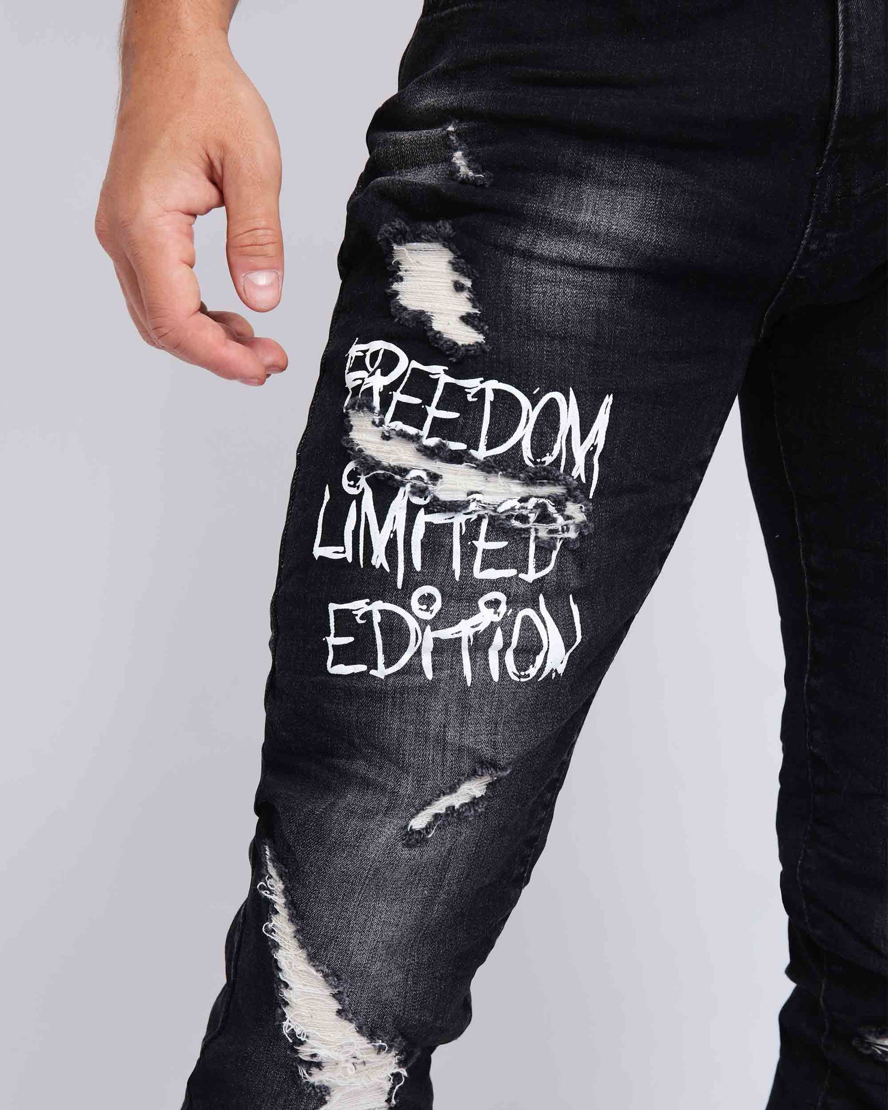 Close-up of LOGEQI black ripped jeans for men with “FREEDOM LIMITED EDITION” white text