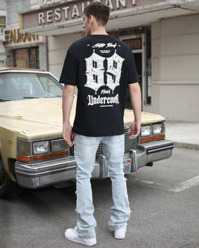 Man wearing LOGEQI's fashionable light wash blue layered ripped baggy jeans and black printed T-shirt with his back turned