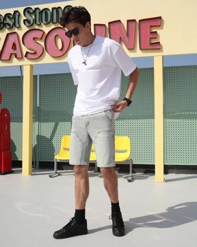 A man wearing LOGEQI's affordable distressed light blue denim jean shorts, paired with sunglasses, black shoes, and a white T-shirt on the street