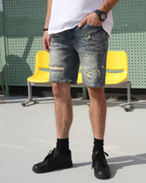 A man wearing LOGEQI's blue ripped denim cargo shorts with white paint splatter, paired with a white T-shirt and black shoes