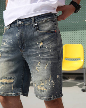 Showing the front details of LOGEQI's men's cargo denim shorts with a ripped design and white paint splatter.