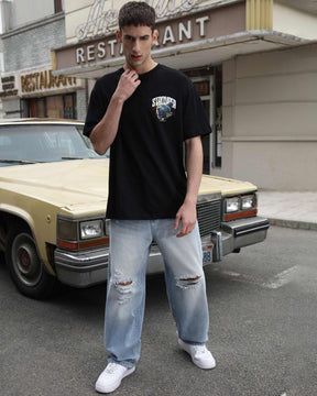 A man styling LOGEQI's blue ripped loose baggy jeans with a printed black T-shirt and white sneakers.