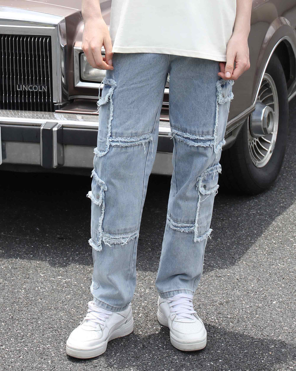 A man styling LOGEQI's men's fringed edge, ripped, distressed baggy jeans with a white T-shirt and white sneakers, with a car in the background 