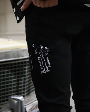 Black jeans featuring white embroidered phrases, hand in pocket, urban style